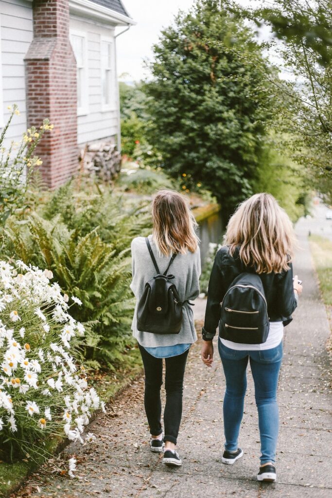 two children walking on sidewalk with black backpacks