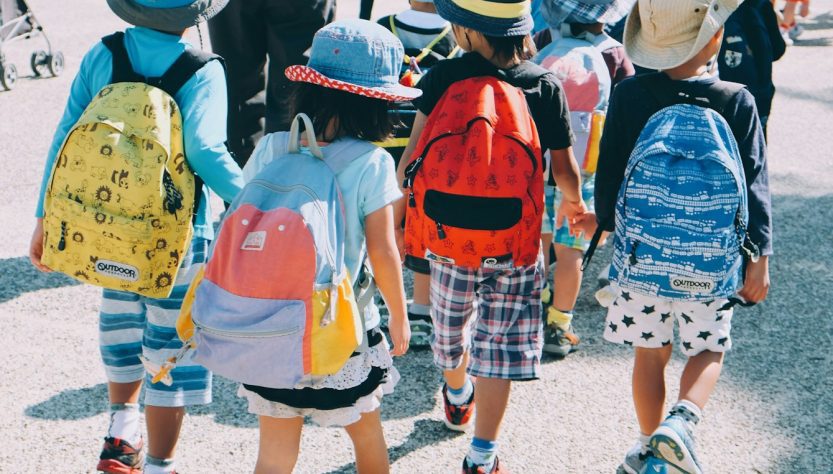 group of people wearing white and orange backpacks walking on gray concrete pavement during daytime