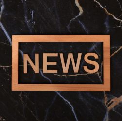 Wooden text of 'news' outlined on a dark, marbled surface, creating a striking contrast.