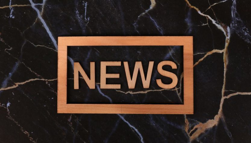 Wooden text of 'news' outlined on a dark, marbled surface, creating a striking contrast.