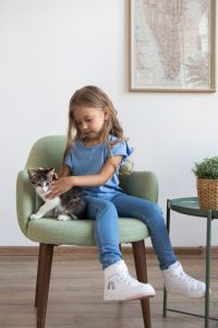 Child sitting with a domestic cat on an armchair, embracing a joyful moment indoors.