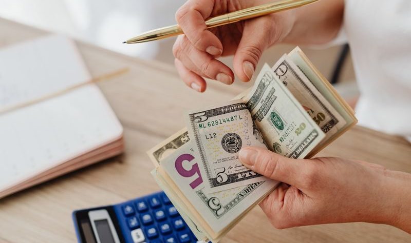 Change Your Money Mindset to Unlock Financial Success and Stability 1 Woman counting money with calculator and receipts on a desk, planning budget.
