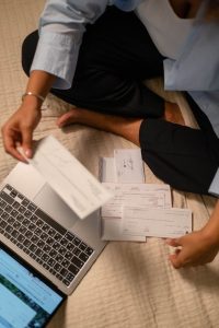 Change Your Money Mindset to Unlock Financial Success and Stability 2 An adult organizing cheques and using a laptop indoors for financial tasks.