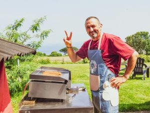Stay Cool while cooking this Summer 2 Man grilling hot dogs and giving peace sign